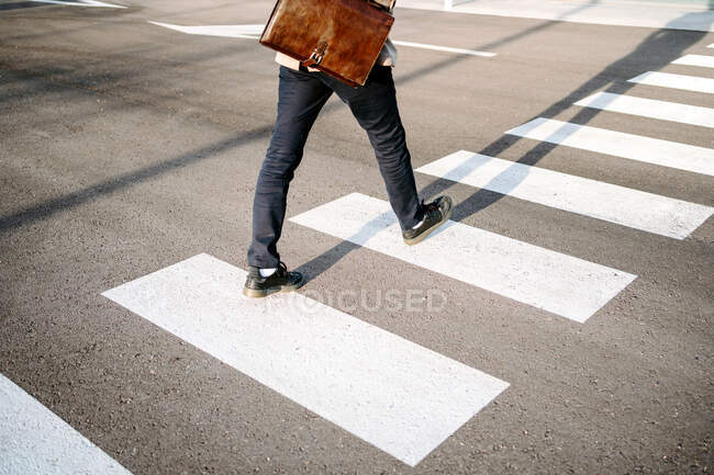 Crop unrecognizable male entrepreneur in stylish outfit walking on crosswalk on sunny day in city — Stock Photo