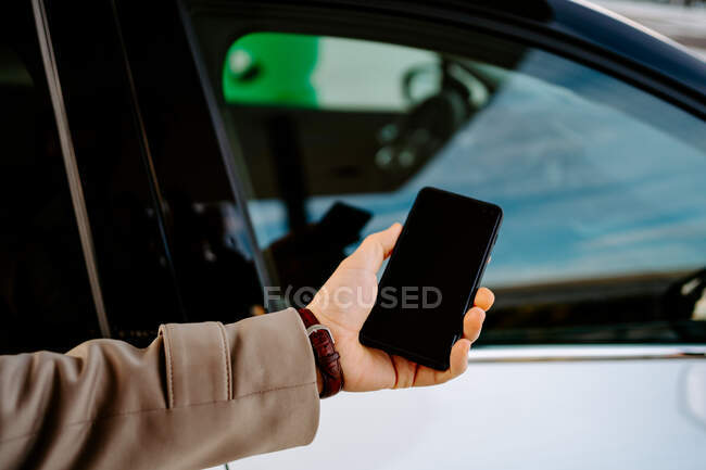 Чоловік-підприємець розблоковує двері сучасного автомобіля зі смартфоном під час використання програми дистанційного керування — стокове фото