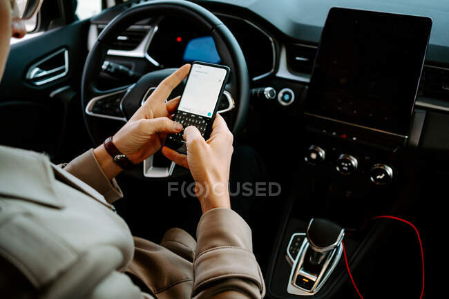 Crop unrecognizable male entrepreneur sitting on driver seat in luxury automobile and browsing mobile phone — Stock Photo