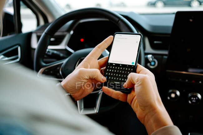 Crop imprenditore maschile irriconoscibile seduto sul sedile del conducente in auto di lusso e la navigazione cellulare — Foto stock
