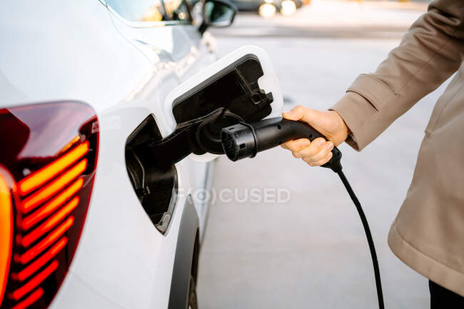Crop of stylish male entrepreneur browsing smartphone while standing at petrol station and refueling automobile — Stock Photo