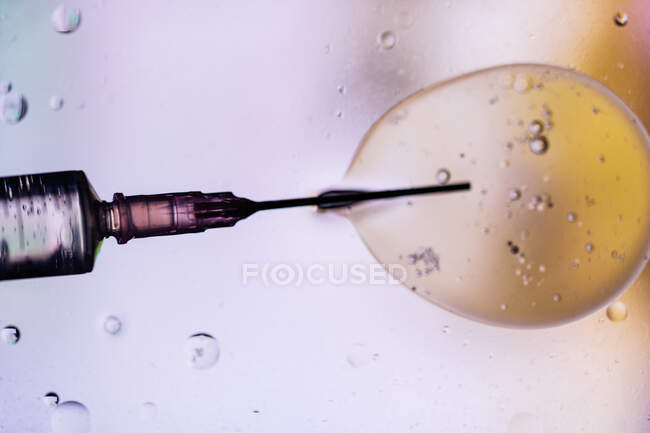 Gros plan de l'aiguille de la seringue remplie du vaccin du virus injecté dans la cellule sur fond flou — Photo de stock