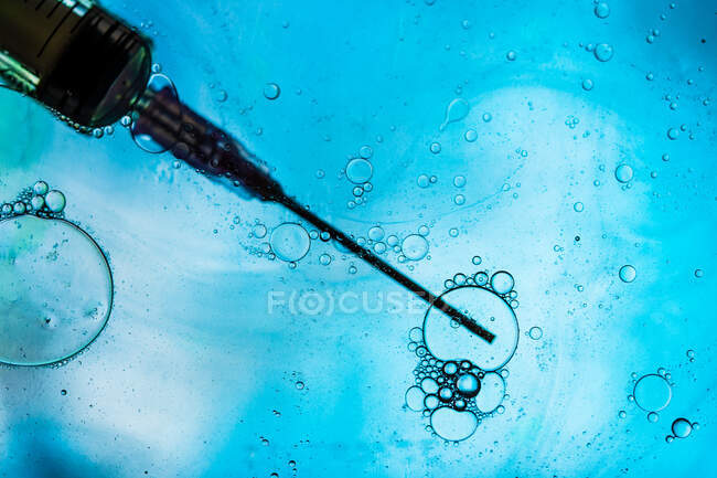 Closeup of needle of syringe filled with vaccine from virus injected in cell on blurred background — Stock Photo