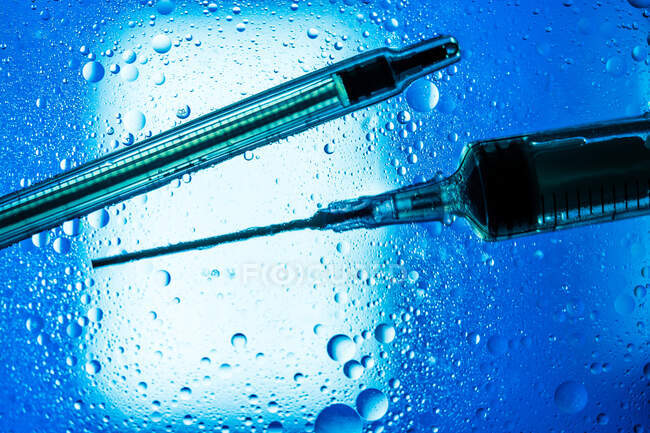 Closeup of syringes with vaccine placed on wet glass table with droplets illuminated by blue light — Stock Photo