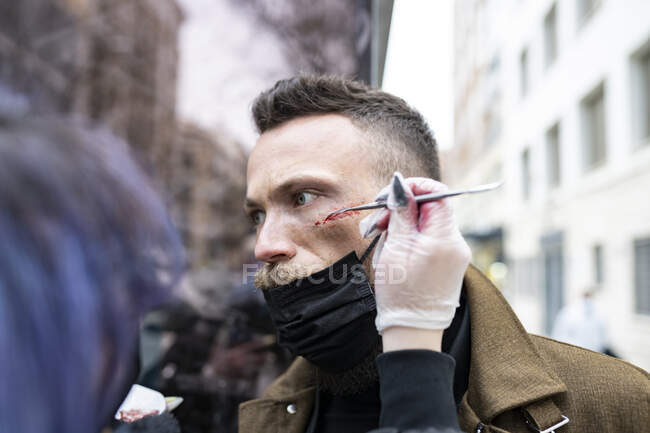 Primer plano de un artista de maquillaje irreconocible poniendo maquillaje en la cara de un hombre hipster - foto de stock