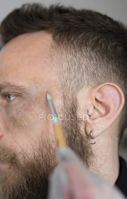 Close-up of an unrecognizable makeup artist putting makeup on a hipster man's face — Stock Photo