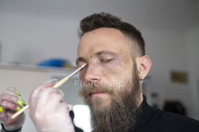 Close-up de um artista de maquiagem irreconhecível colocando maquiagem no rosto de um homem hipster — Fotografia de Stock
