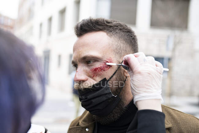 Primer plano de un artista de maquillaje irreconocible poniendo maquillaje en la cara de un hombre hipster - foto de stock