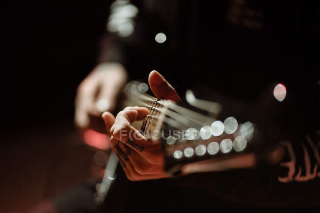 Guitarrista de vista lateral tocando la guitarra eléctrica mientras actúa en estudio oscuro con luz roja - foto de stock