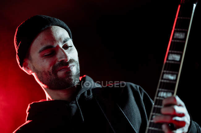 Bajo ángulo de guitarrista de rock tocando la guitarra eléctrica mientras se realiza en estudio oscuro con luz roja - foto de stock