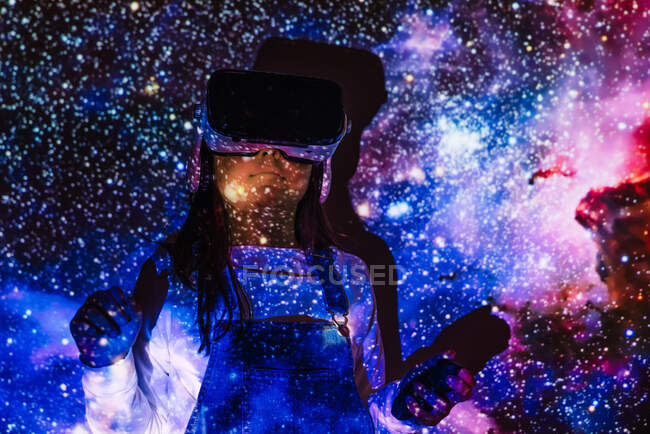 Невпізнавана дівчина в повсякденному одязі і VR навушники отримують новий досвід і торкаються віртуального об'єкта в кімнаті з кольоровим проектором освітлення — стокове фото