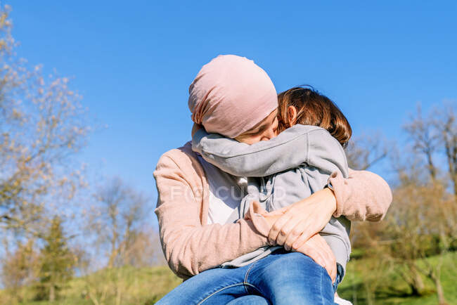 Happy mother with cancer wearing pink head scarf hugging little daughter on green park — Stock Photo
