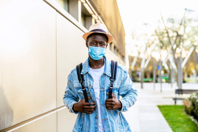 Anonymous young African American male in sterile mask and casual wear looking at camera on city walkway during COVID 19 pandemic — Stock Photo