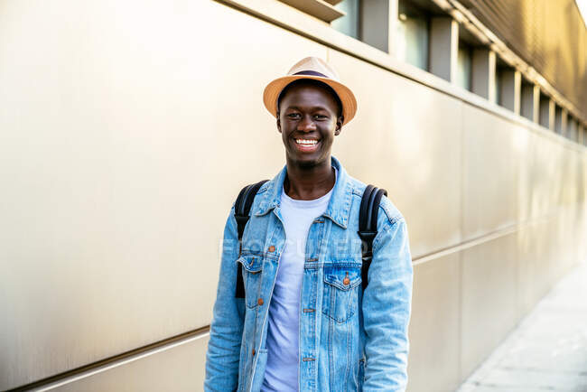 Cheerful young black man in denim jacket looking straight ahead with a toothy grin in daylight. — Stock Photo