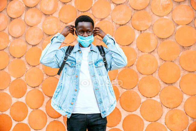Irriconoscibile giovane contemplativo maschio nero in giacca di denim e maschera respiratoria distogliendo lo sguardo durante la pandemia di coronavirus — Foto stock