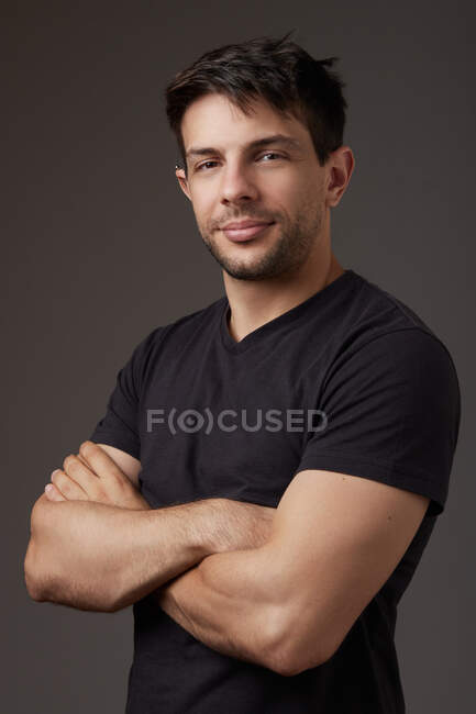 Homme en chemise noire avec bras croisés regardant la caméra sur fond gris en studio — Photo de stock