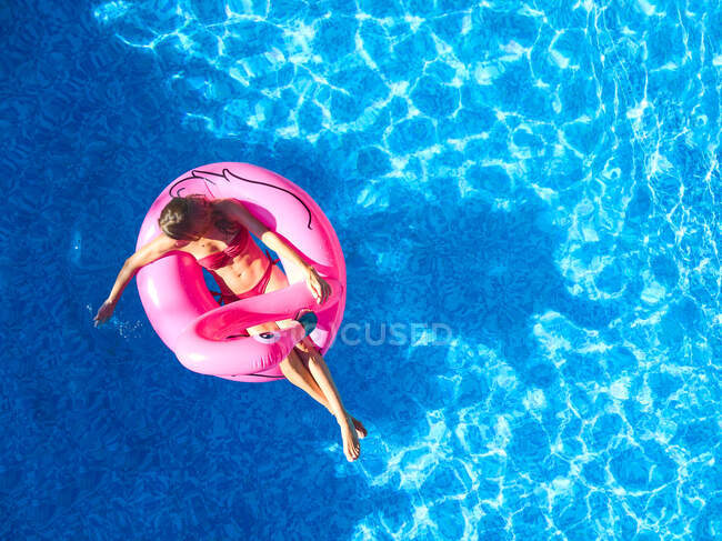 Dall'alto della donna in costume da bagno galleggiante su anello gonfiabile rosa in acqua blu chiaro della piscina all'aperto durante le vacanze estive — Foto stock