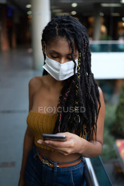 Портрет привабливої жінки африканського латину, одягненої в феймаск і за допомогою смартфона в торговому центрі (Колумбія). — стокове фото