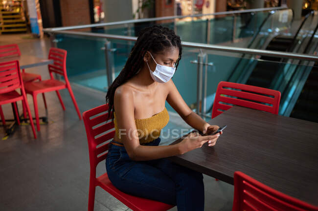 Portrait of attractive young afro latin woman wearing a facemask and using smartphone in a commercial mall, Colombia — Stock Photo