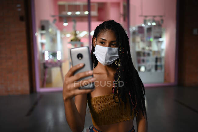 Portrait of attractive young afro latin woman wearing a facemask and doing a videocall on smartphone in a commercial mall, Colombia — Stock Photo