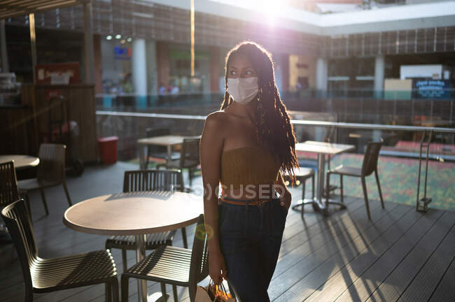 Backlighting portrait of attractive young afro latin woman in facemask and holding shopping bags in commercial mall, Colombia — Stock Photo