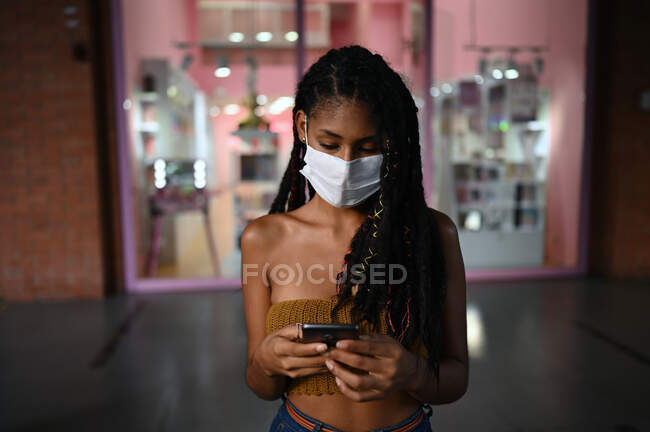 Портрет привабливої жінки африканського латину, одягненої в феймаск і за допомогою смартфона в торговому центрі (Колумбія). — стокове фото
