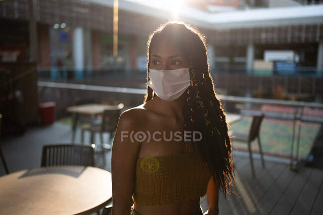 Portrait rétroéclairé d'une jolie jeune femme afro latine en masque et tenant des sacs à provisions dans un centre commercial, Colombie — Photo de stock
