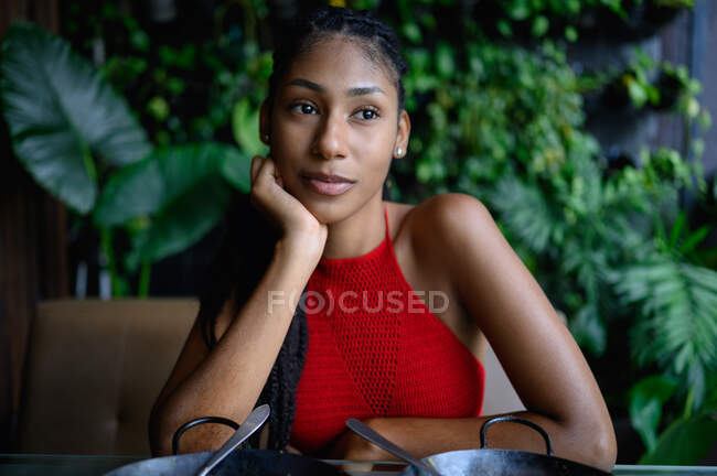 Ritratto di contemplativa giovane donna afro latino con dreadlocks in un top rosso all'uncinetto seduto sul tavolo, Colombia — Foto stock