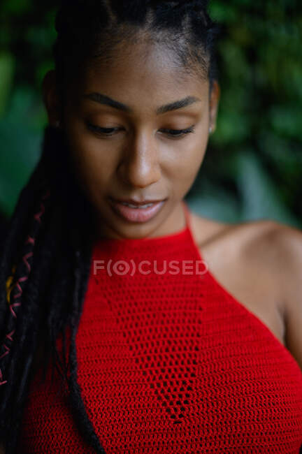 Retrato de mujer latina afro joven con rastas en un top rojo de ganchillo mirando hacia abajo, Colombia - foto de stock