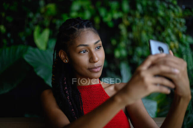 Портрет привабливої жінки африканського латину з дредами у червоному крохті, використовуючи смартфон у ресторанному столі (Колумбія). — стокове фото