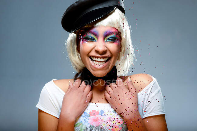 Chica rubia con pelo corto y maquillaje colorido divirtiéndose con confeti - foto de stock