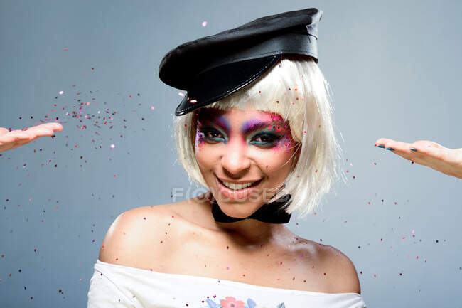 Chica rubia con pelo corto y maquillaje colorido divirtiéndose con confeti - foto de stock