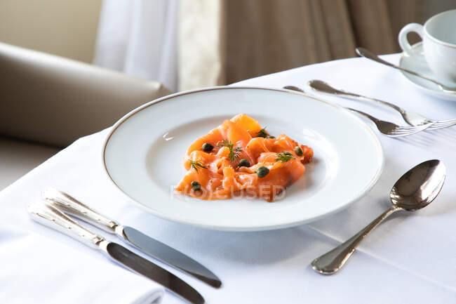 D'en haut de savoureux saumon fumé en tranches appétissant servi dans une assiette avec des câpres et des herbes dans un élégant restaurant — Photo de stock