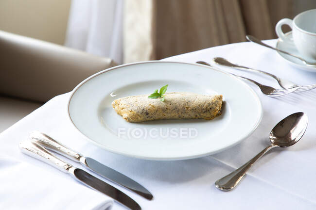 From above of delicious sweet rolled pancake with chocolate and mint leaf placed on white plate served on table white coffee cup and cutlery during breakfast in restaurant — Stock Photo
