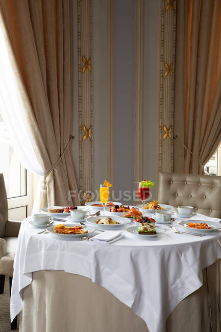 Divers plats colorés et jus servis sur la table ronde pendant le petit déjeuner dans l'élégant restaurant de l'hôtel dans la matinée ensoleillée — Photo de stock