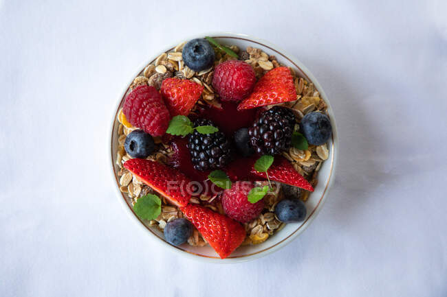 Top view of appetizing muesli bowl decorated with various fresh berries and mint leaves served on white table in morning — Stock Photo