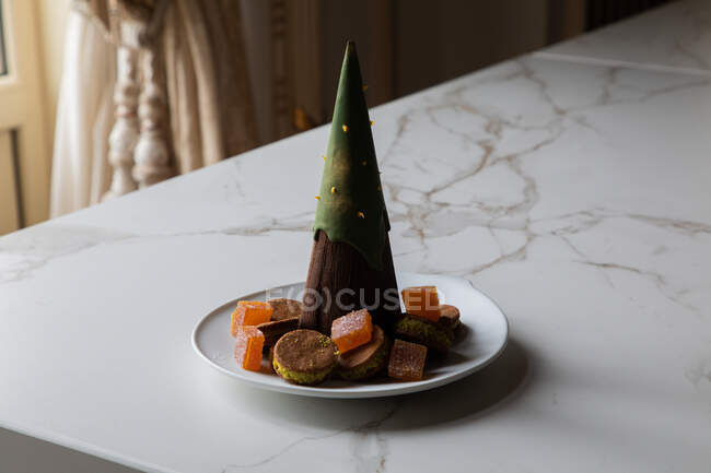 Weihnachtsbaumförmiges Schokoladendessert auf Teller mit verschiedenen Plätzchen und Marmelade, serviert auf Marmortisch im stilvollen Restaurant — Stockfoto