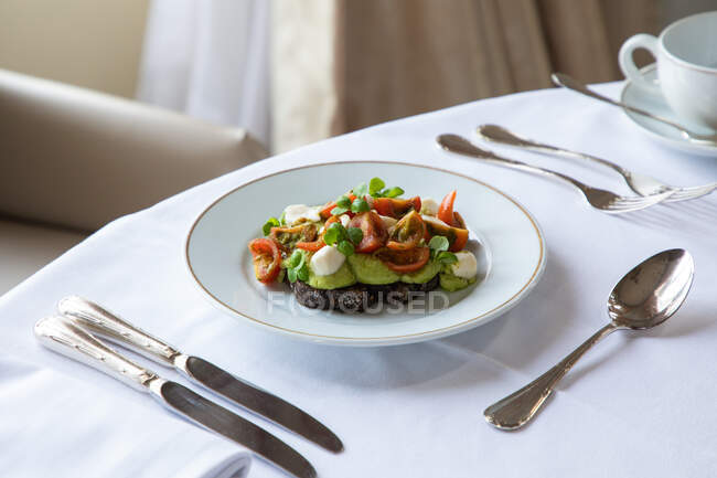 Сверху вкусные тосты с разбитым авокадо, украшенным помидорами черри и сыром, подаваемыми на тарелке в ресторане во время кофе-брейка — стоковое фото
