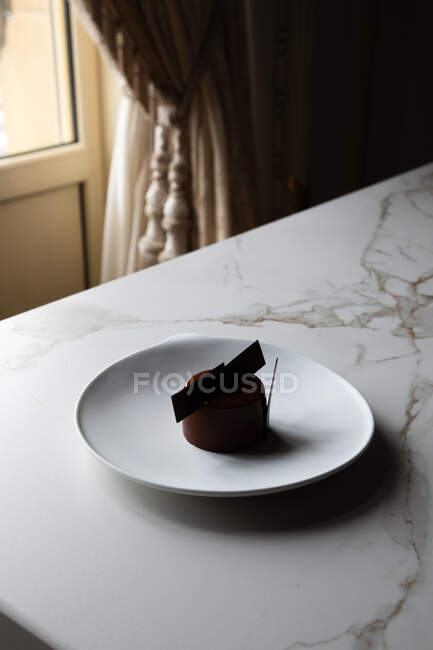 High angle of yummy chocolate glazed cake decorated with edible decoration served on white plate and placed on marble table — Stock Photo