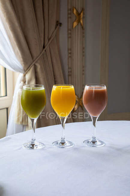 Surtido de coloridos jugos recién exprimidos en elegantes vasos colocados en la mesa en el restaurante - foto de stock