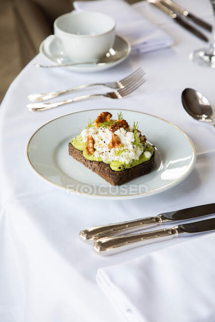 Von oben gesunder Avocado-Toast mit Ricotta und Walnüssen auf weißem Teller und serviert auf dem Tisch im Café während des Frühstücks — Stockfoto