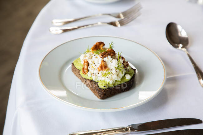 From above of healthy avocado toast with ricotta and walnuts placed on white plate and served on table in cafe during breakfast — Stock Photo