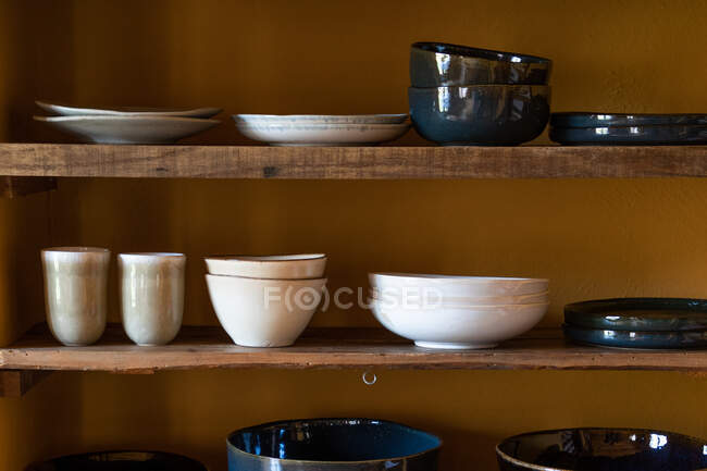Набір різних посуду, що складається з тарілок чашок і чашок, розміщених на дерев'яних полицях — стокове фото