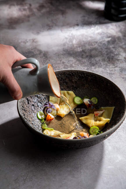 Crop anonymous cook adding broth into bowl with traditional Japanese dumplings while preparing meal in restaurant — Stock Photo
