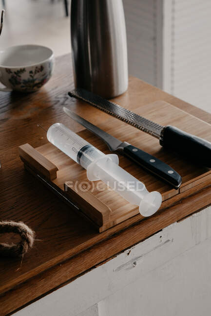 From above of various sharp knives and culinary syringe placed on wooden cutting board in kitchen — Stock Photo