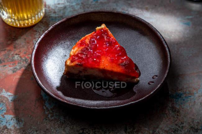 Сверху аппетитный пирог с ягодным вареньем помещен на керамическую тарелку со стаканом напитка со льдом в ресторане — стоковое фото