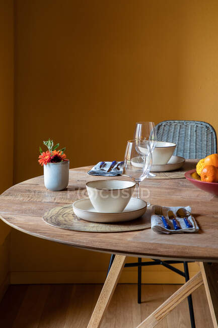 Served table with ceramic bowls on plates with cutlery on napkin near wineglasses and flowers with fruits — Stock Photo