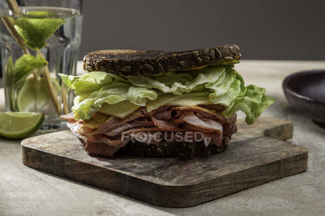 Alto angolo di panino appetitoso con pane fresco croccante sopra le foglie di lattuga e pancetta su tavola di legno — Foto stock