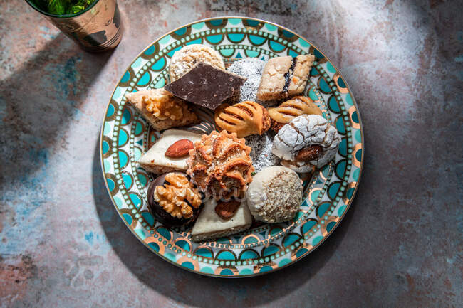 From above of baklava and biscuits with Moroccan peppermint tea near knife and fork placed on table decorated with mint leaves — Stock Photo