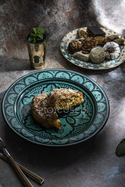 Сверху пахлавы и печенья с марокканским мятным чаем рядом с ножом и вилкой на столе, украшенном листьями мяты — стоковое фото